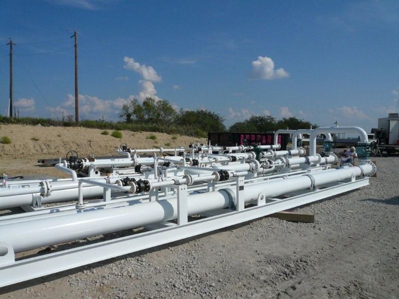 White coated pipeline headers and manifolds staged in a gravel yard