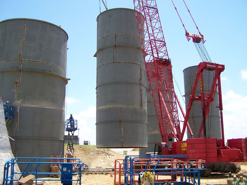 Two large storage silos being set by red and yellow crawler cranes