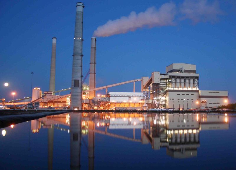 Power plant lit up at night, reflected in the water in front of it