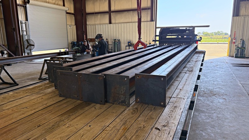 Fabricated steel members loaded on a flatbed trailer inside the shop