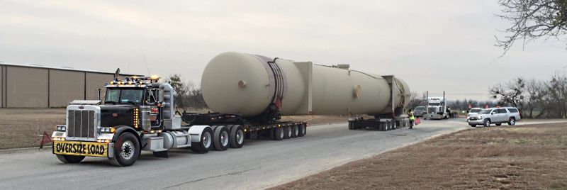 A large pressure vessel strapped to a lowboy trailer leaving the yard
