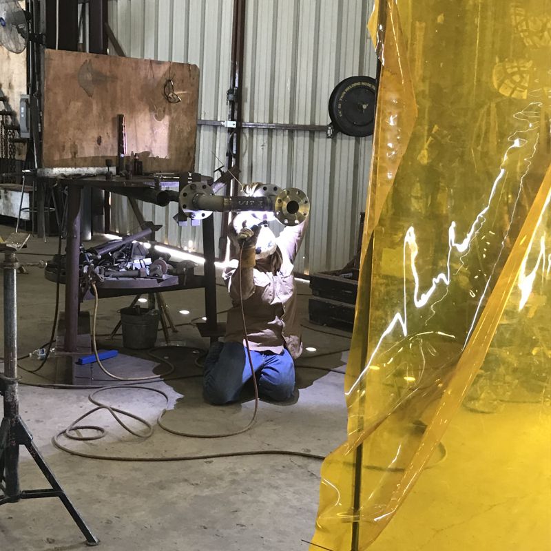 A welder at work behind a yellow weld curtain in the shop
